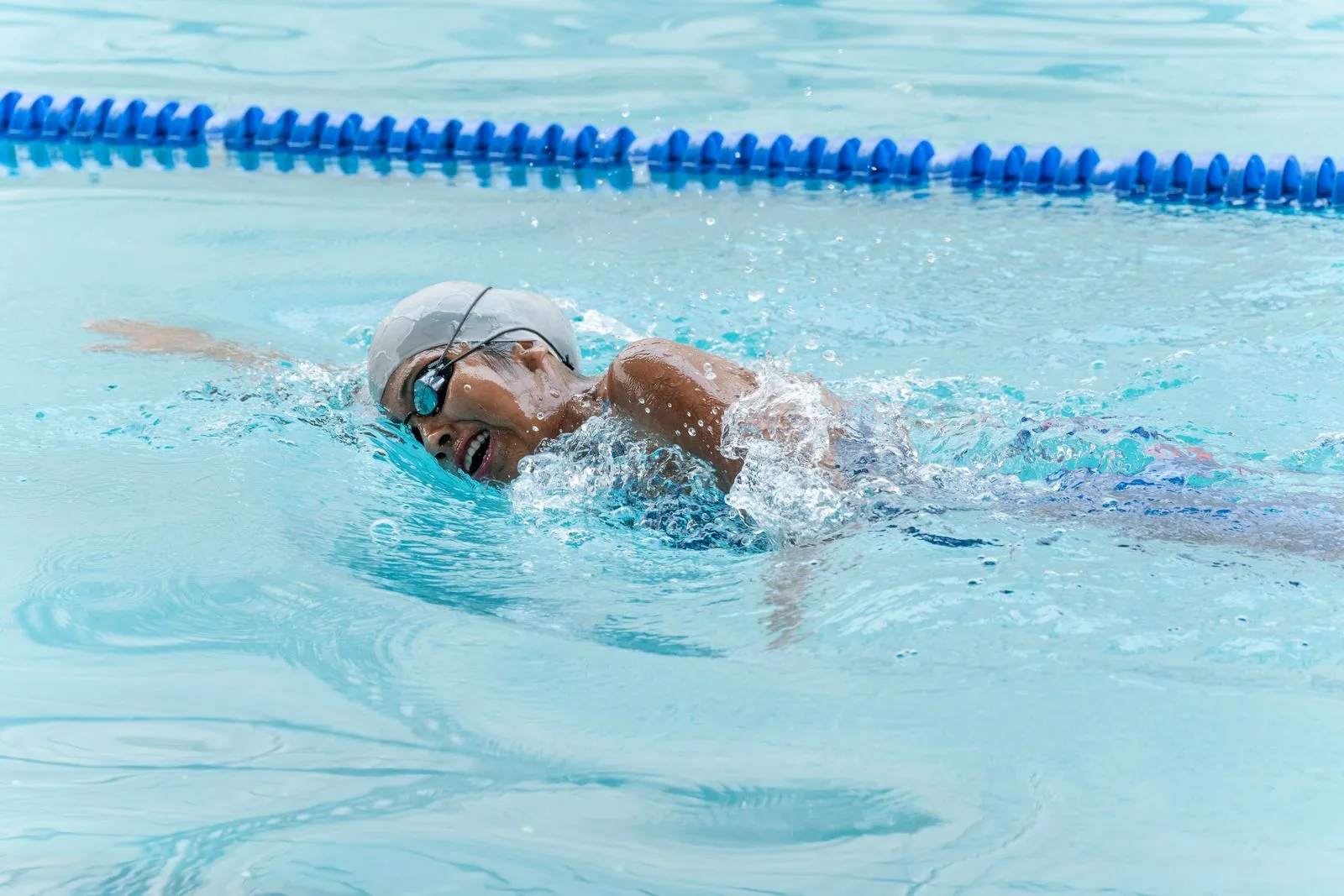 Focused female swimmer practicing freestyle in a swimming pool with swim cap and goggles.