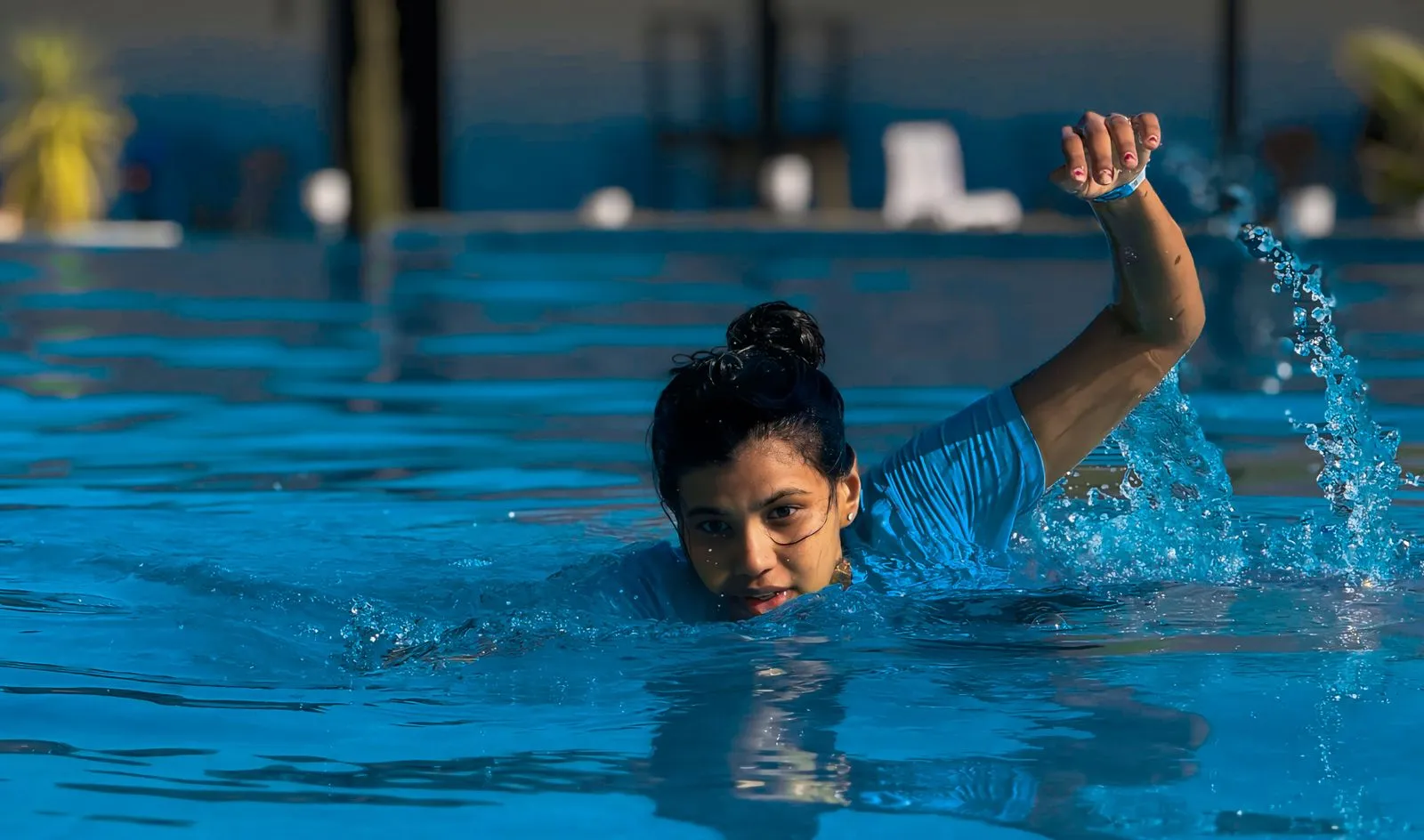 A woman swims energetically in an outdoor pool, enjoying a sunny day.